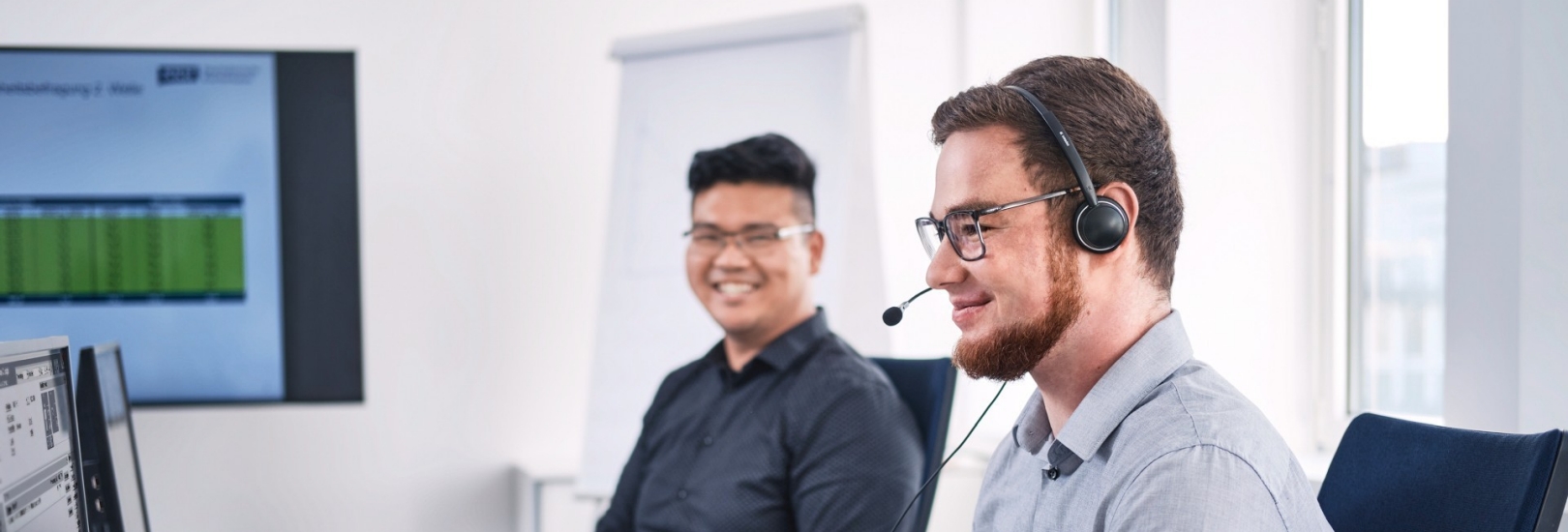 Zwei Kollegen im Büro mit Headset und Lächeln